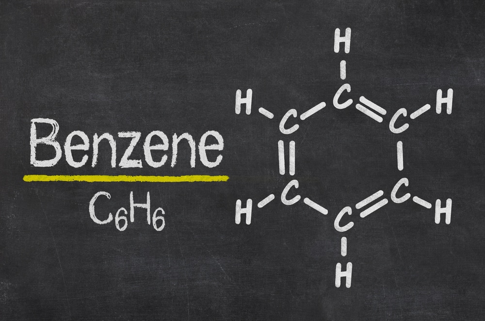 Image of a chalkboard with the word 'Benzene' written in large, white chalk letters, underlined in yellow. Below 'Benzene' is its chemical formula 'C6H6.' To the right, a hexagonal diagram represents the benzene molecule, showing alternating single and double bonds between carbon atoms, with hydrogen atoms attached to each carbon.