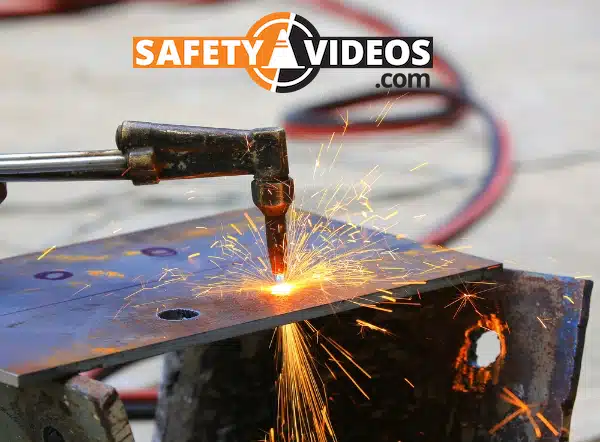 A close-up photo of a cutting torch in action, with bright sparks flying as it cuts through a steel plate. The background is blurred, highlighting the precision of the cut and the intensity of the work. The logo 'SAFETYVIDEOS.COM' is prominently displayed in the upper right corner, suggesting a focus on safety in industrial procedures.