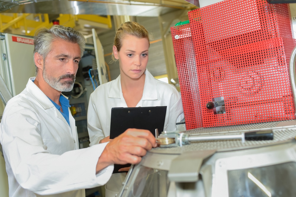 Two people in lab coats looking at a machine.