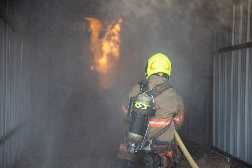 A firefighter with a hose in a warehouse.