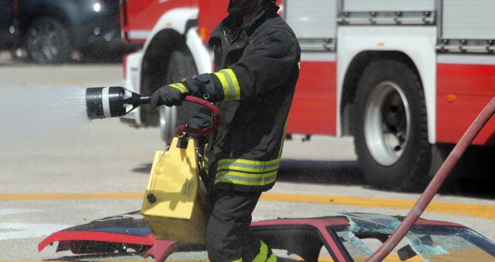 A firefighter spraying water on a car.