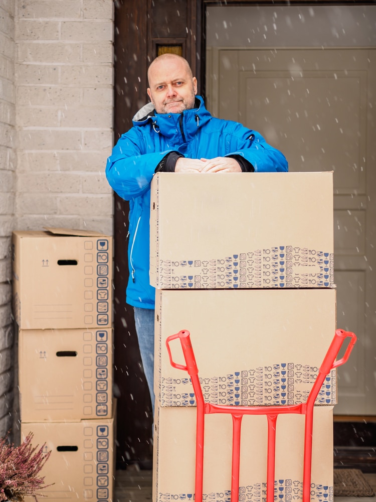 A man in a blue jacket holding a cart full of boxes.