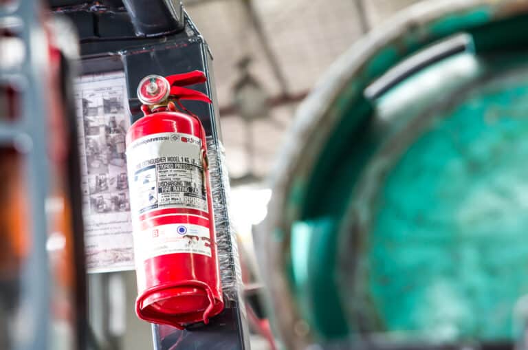 A fire extinguisher strapped to a forklift in a warehouse.