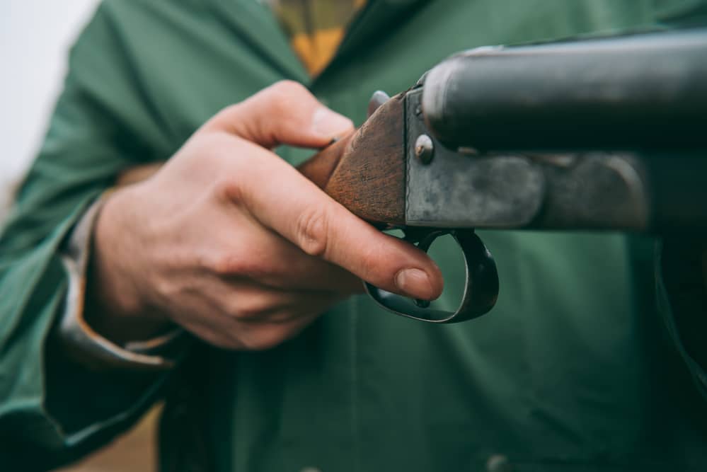 A man in a green jacket holding a shotgun.