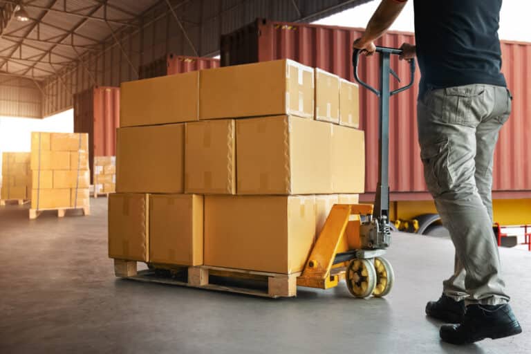 A man pushing a pallet of boxes in a warehouse.