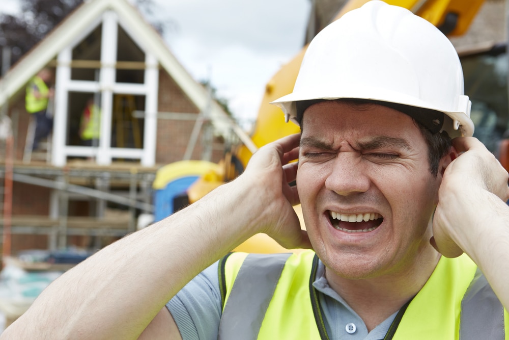 A construction worker covering his ears in front of a construction site.