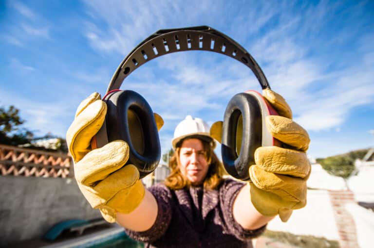 A woman is holding a pair of ear defenders.