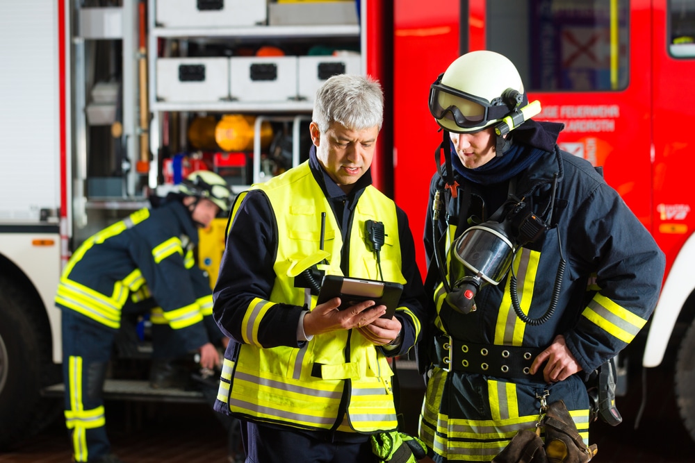 Two firefighters looking at a tablet in front of a fire truck.