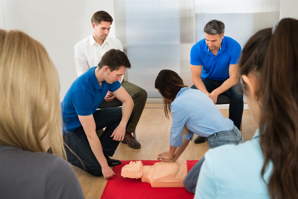 A group of people sitting around an ecg dummy, going through first aid training