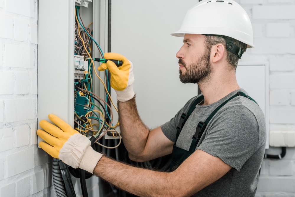 A man in a hard hat is working on an electrical panel.