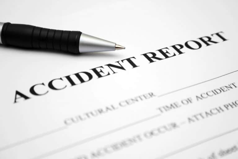 A close-up image of the top section of an 'Accident Report' form with a black pen lying diagonally across it. The form includes fields for 'Cultural Center', 'Time of Accident', and a prompt to 'ATTACH PHOTOGRAPH OF ACCIDENT OCCUR'