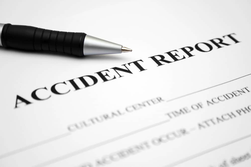 A close-up image of the top section of an 'Accident Report' form with a black pen lying diagonally across it. The form includes fields for 'Cultural Center', 'Time of Accident', and a prompt to 'ATTACH PHOTOGRAPH OF ACCIDENT OCCUR'