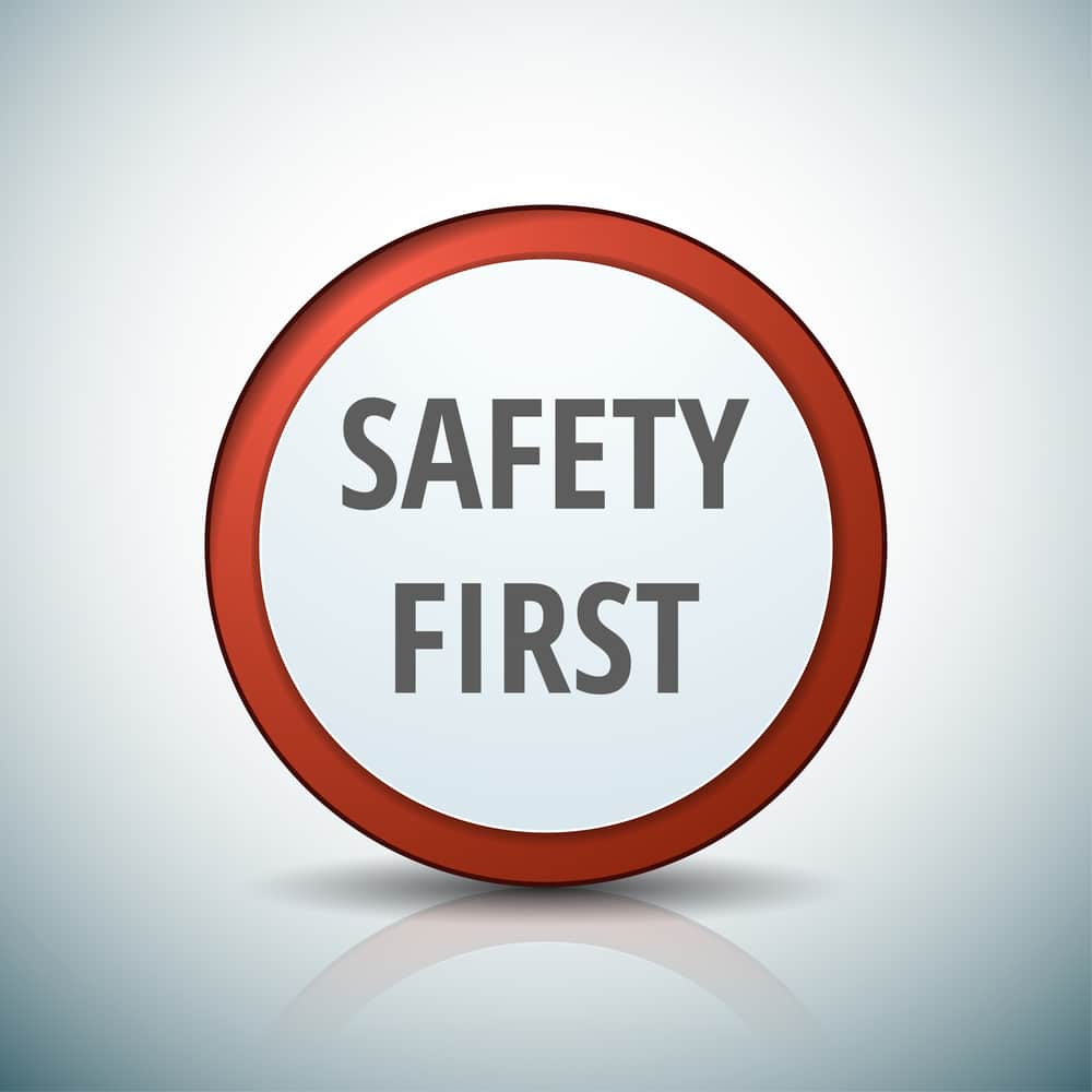 A bold, red circular badge with the words 'SAFETY FIRST' prominently displayed in capital letters at the center against a light grey background, creating a clear and impactful message about the importance of safety in the workplace.